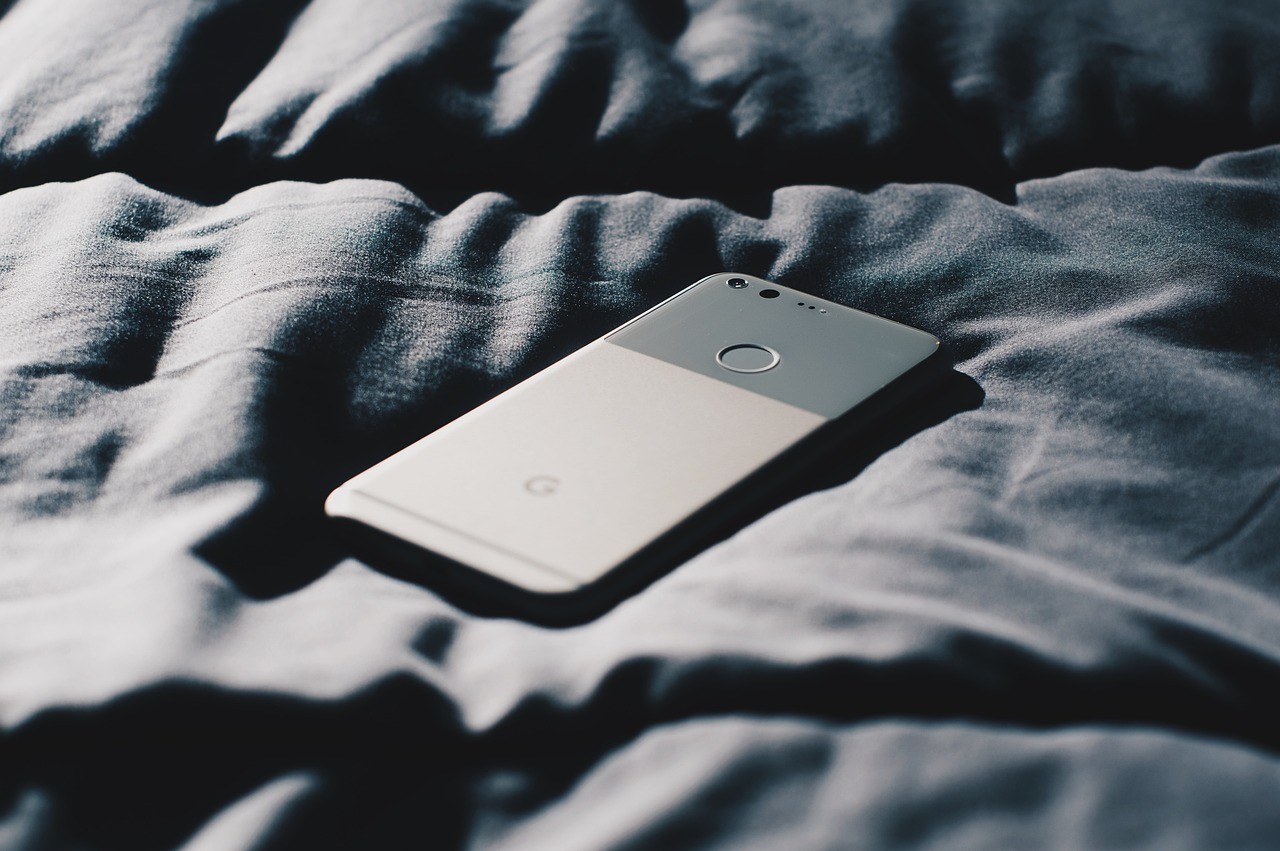 Téléphone au bord d'un lit, écran allumé dans l'obscurité, la nuit