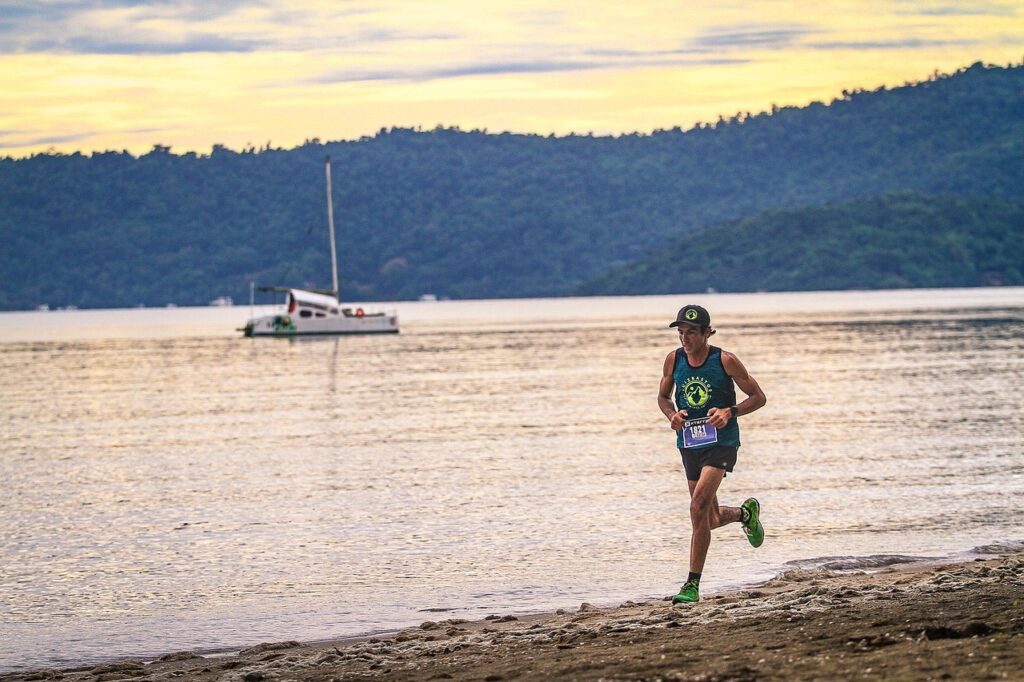 Un coureur d'ultra-trail progresse seul le long d'une plage au crépuscule, dossard de course visible