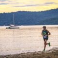 Un coureur d'ultra-trail progresse seul le long d'une plage au crépuscule, dossard de course visible