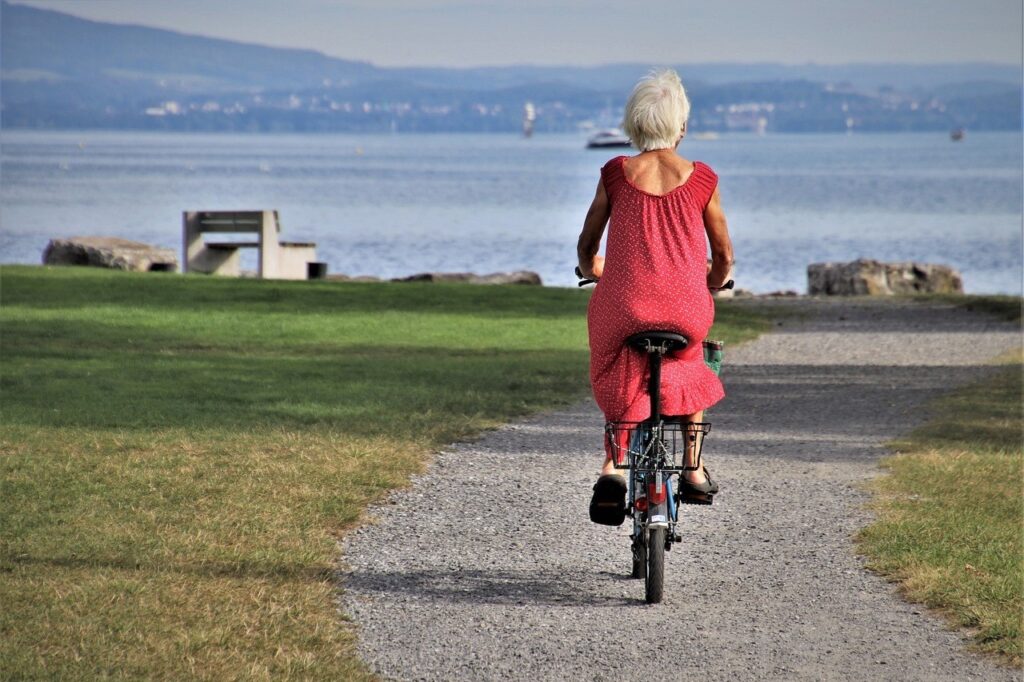 Femme senior à vélo sur un chemin au bord d'un lac, de dos, par une journée ensoleillée