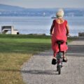 Femme senior à vélo sur un chemin au bord d'un lac, de dos, par une journée ensoleillée
