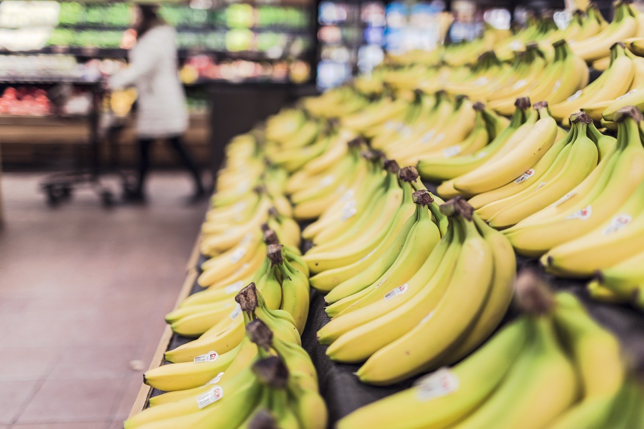Rayon de fruits et légumes frais dans un supermarché, avec une personne faisant ses courses en arrière-plan
