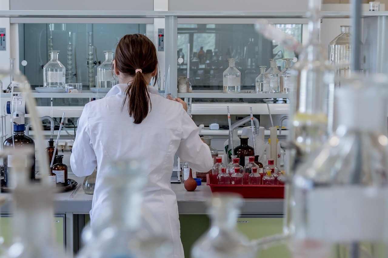 Chercheuse de dos dans un laboratoire, paillasse de verrerie scientifique, scène documentaire