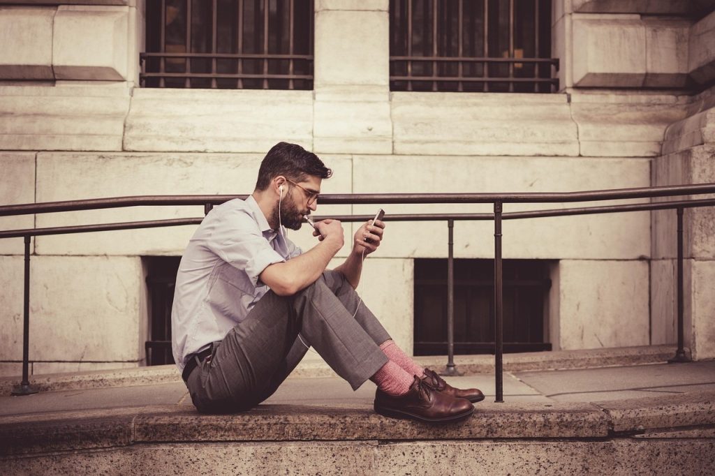 Homme assis dans la rue, en train de consulter son téléphone, lumière naturelle