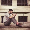 Homme assis dans la rue, en train de consulter son téléphone, lumière naturelle